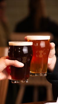 pexels-photo-34530775-34530775 Two people toasting with pints of beer in a cozy pub setting, showcasing camaraderie and celebration.